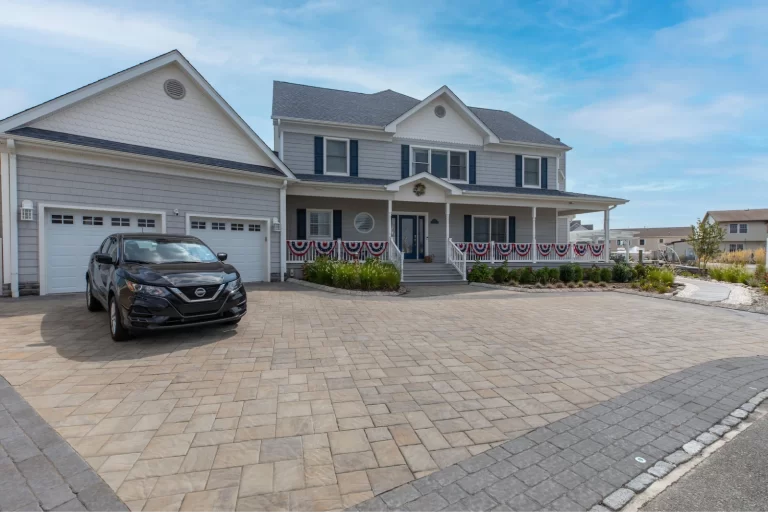Two-story gray house with three-car garage, car parked in driveway, and patriotic bunting on porch railing.