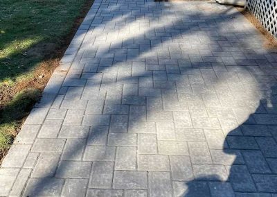 Gray stone walkway beside a house, with grass and a black metal pool in the background.