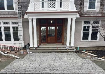 Stone walkway leads to a large wooden front door of a house with white columns and balcony.