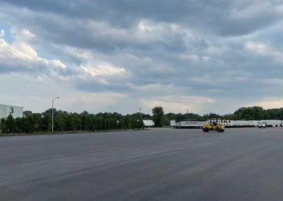 A large empty parking lot with a few trucks and a yellow vehicle under a cloudy sky.