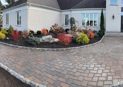 A newly paved stone walkway curves to the entrance of a white brick house with fresh landscaping.