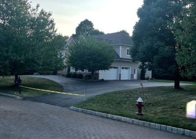 A suburban house with a driveway, yellow caution tape, trees, and a red fire hydrant by the street.