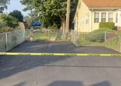 Yellow caution tape blocks the entrance to a fenced yard beside a yellow house with trees in the background.