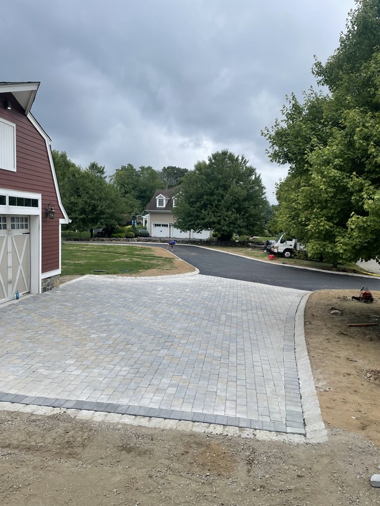 Freshly paved stone driveway in front of a red house with trees and cloudy sky in the background.